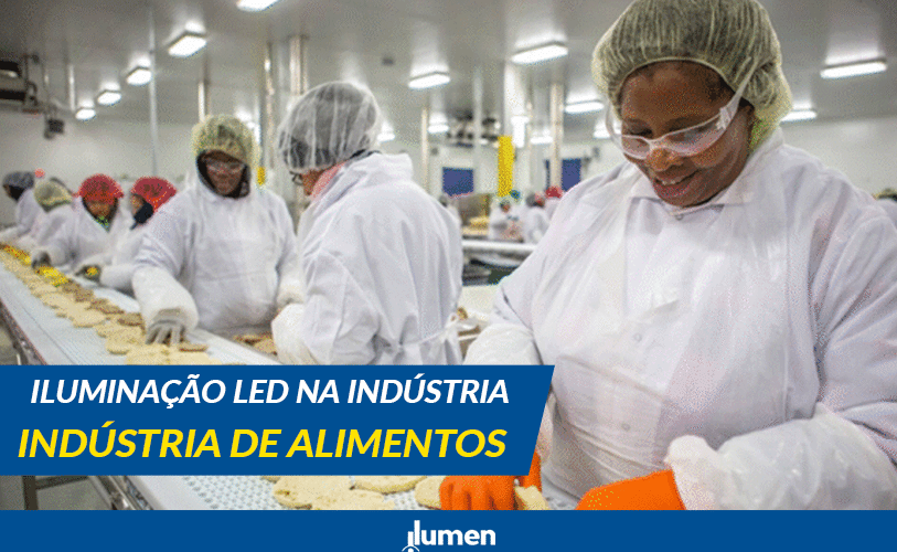 "Trabalhadores da indústria de alimentos em linha de produção, usando equipamentos de proteção e uniformes brancos, sob iluminação LED em ambiente industrial."