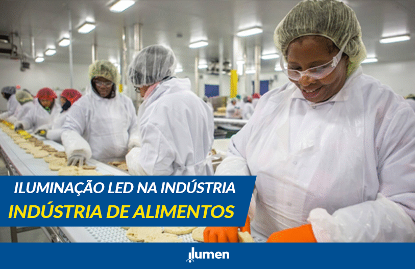 "Trabalhadores da indústria de alimentos em linha de produção, usando equipamentos de proteção e uniformes brancos, sob iluminação LED em ambiente industrial."