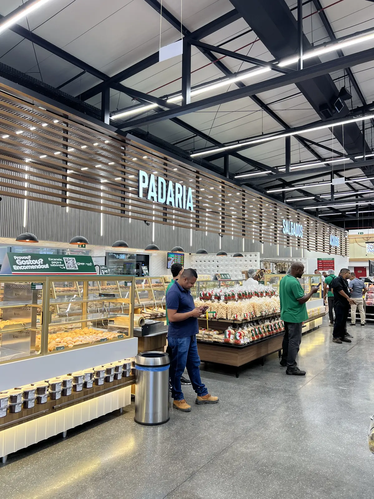 Área de padaria de supermercado com balcões de produtos e luminárias sobre o atendimento